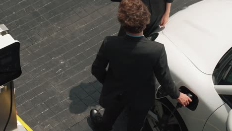 Progressive-businessman-and-businesswoman-leaning-on-EV-car-and-charging-point.