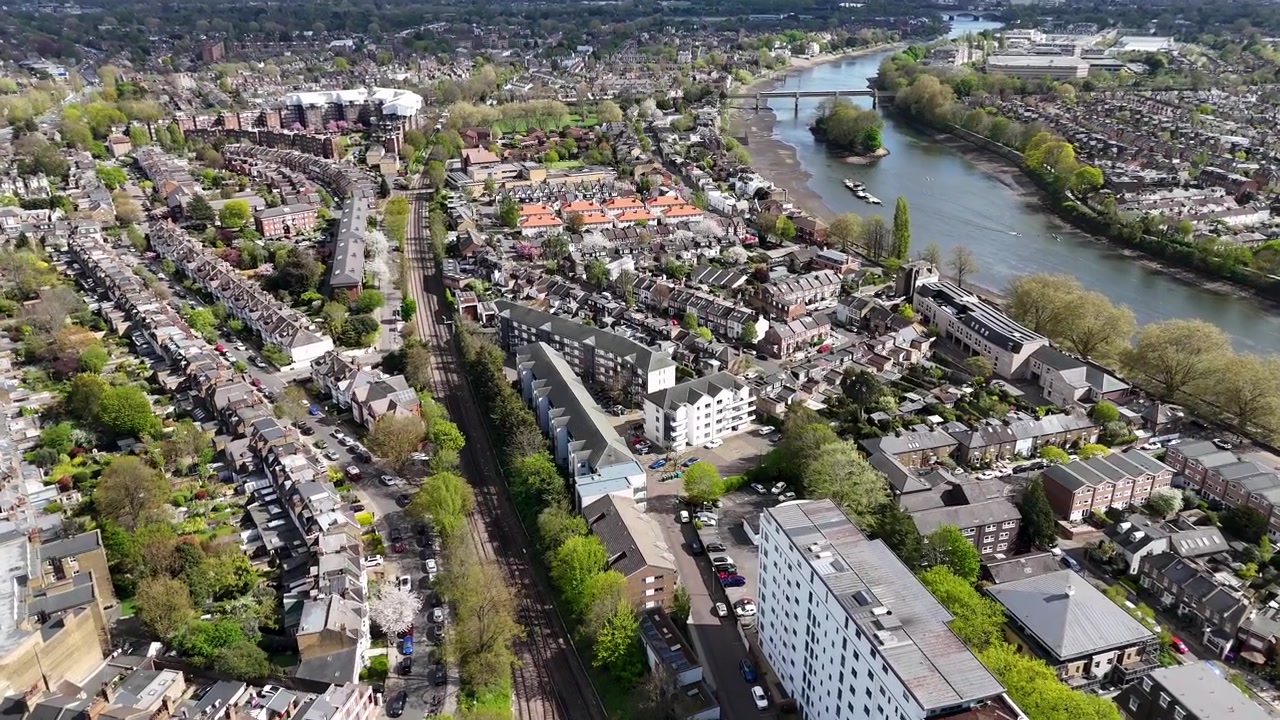 Toits d'une banlieue riveraine verdoyante s'étendant vers un méandre de la rivière, avec un pont lointain et la campagne ouverte à l'horizon