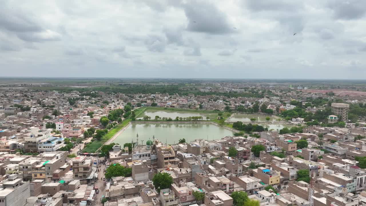 Ripresa aerea con drone in movimento all'indietro sulla città di Mirpur Khas con lo Stagno Centrale nel Sindh, Pakistan, in una giornata nuvolosa.