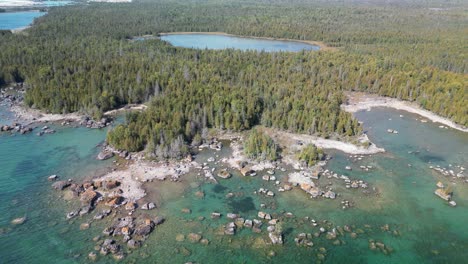 aerial descent pan of rocky forested coastline and inland lake, summer, lake huron