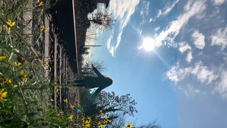 young-girl-running-and-jumping-along-an-abandoned-railroad,-blue-sky-with-clouds-in-the-background,-and-some-yellow-flowers-in-the-foreground