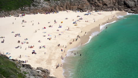 aerial view of porthcurno beach in cornwall full of tourists, swimmers, surfers and families having fun on a beautiful spring sunny day