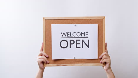 woman's hand shows the paper on board with the word welcome open in white studio background with copy space