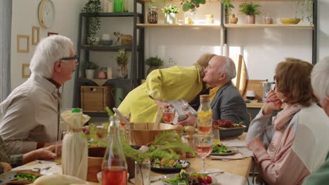 Elderly-Woman-Giving-Birthday-Present-to-Husband-at-Dinner-with-Friends