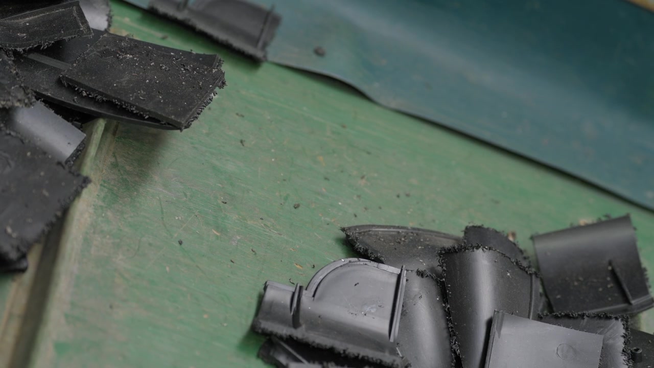 Close up of broken black plastic pieces and dust scattered across worn green factory conveyor belt