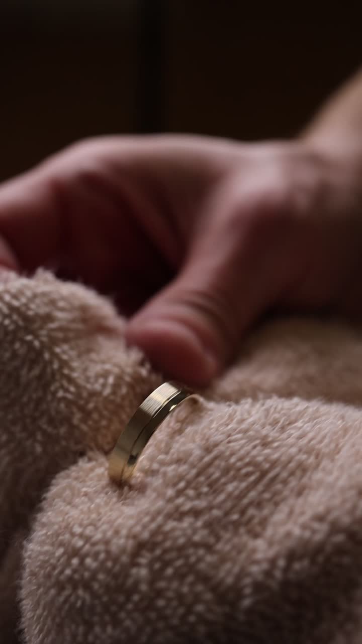 Primo piano della mano che pulisce un anello d'oro con un panno morbido.