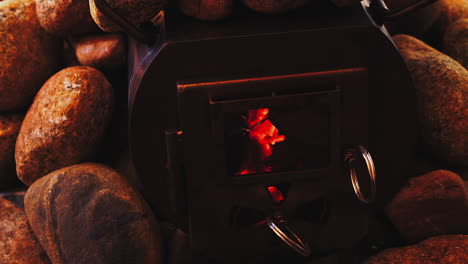 wood coals glow orange in steel wood stove surrounded by hot rocks