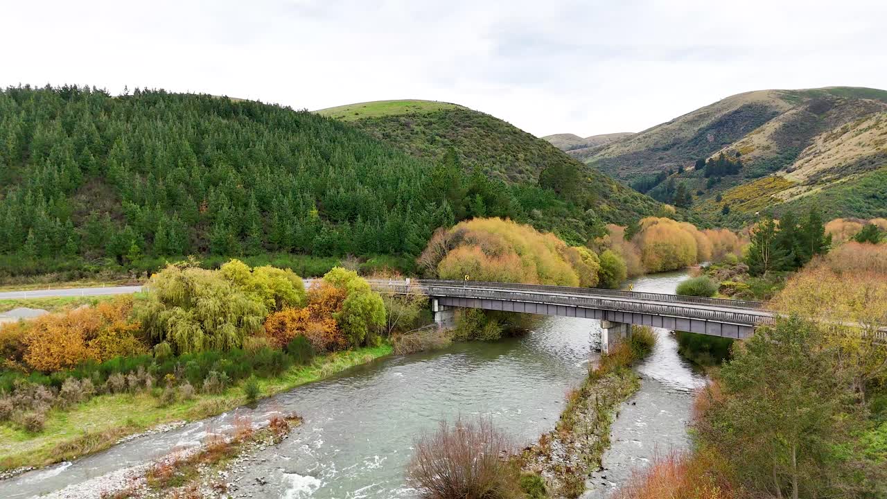 Aerial footage captures a serene bridge over a river surrounded by lush greenery and rolling hills in Lake Tekapo