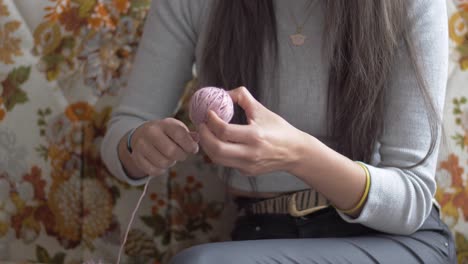 Woman-holds-back-of-yarn,-wraps-up-pink-yarn-from-larger-spool