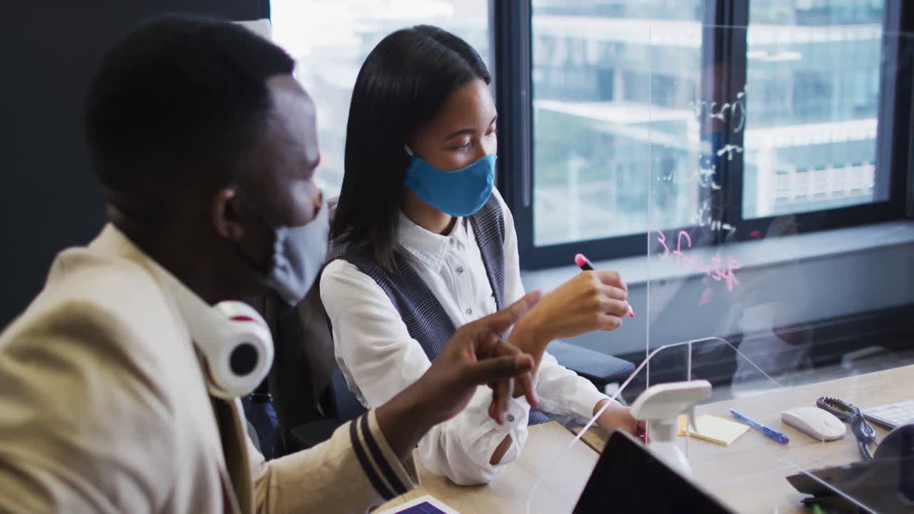 African american man and asian woman writing on glass board at modern office