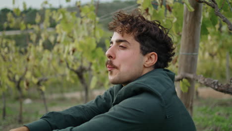 Relaxed-farmer-eating-grapes-at-plantation-under-grapevine-bush-vertical-closeup