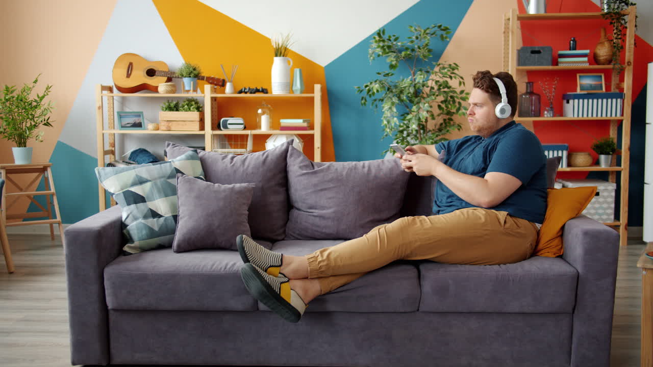 헤드폰과 전화로 소파에서 휴식을 취하는 남자