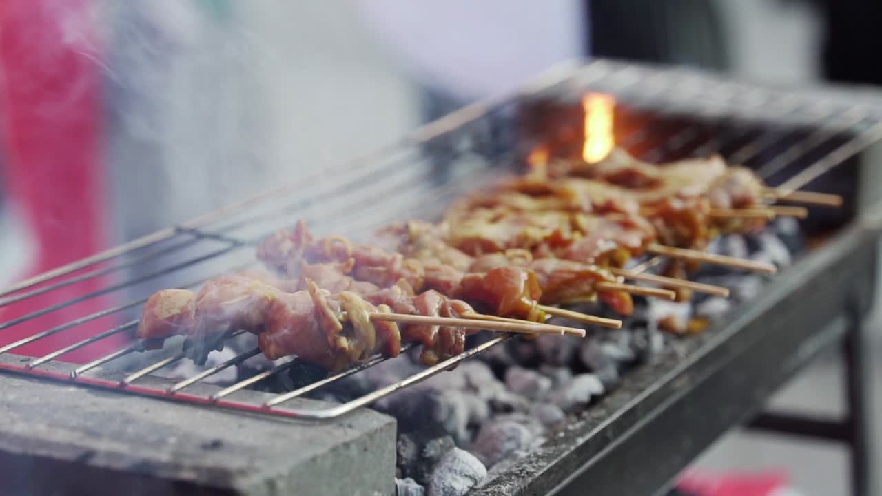 Marinated chicken skewers cooking on open coal grill at market