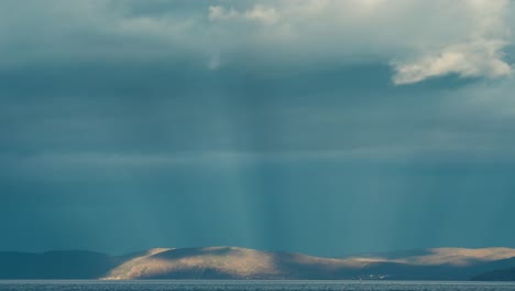 inverted god rays pierce through the thick clouds above the fjord and the land