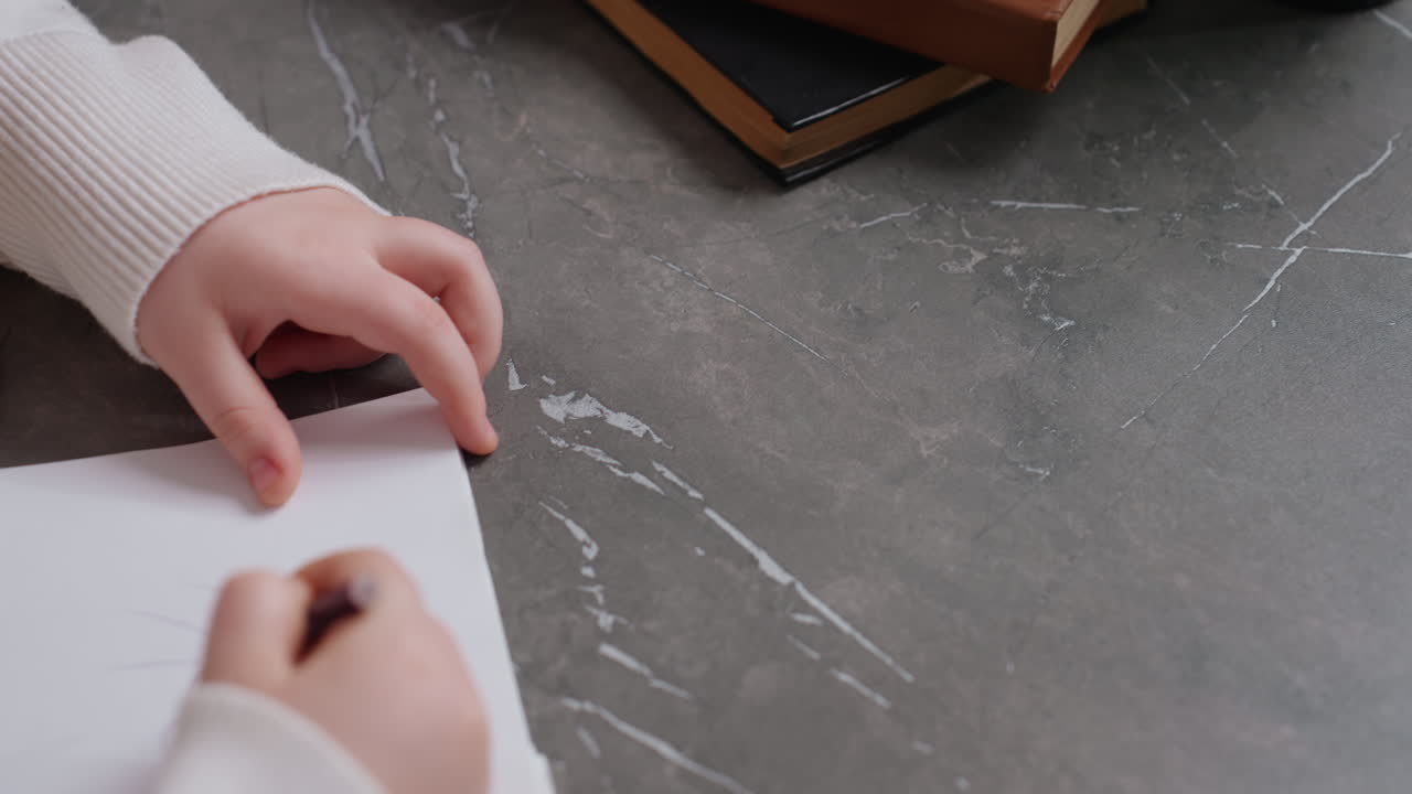 Hands holding purple pencil during learning session with girl, books and plant on desk, symbolizing education, teaching, concentration, discipline, parenting, childhood creativity, guidance