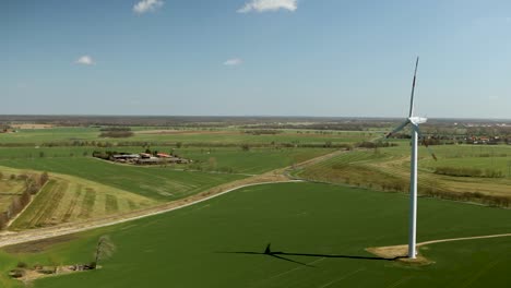 een enkele windturbine in een groen landelijk landschap op een heldere dag, lange schaduwen op de grond, luchtbeeld