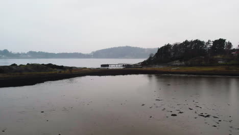 Flying-Towards-a-Jetty-at-Lake,-Misty-Nordic-Landscape,-Low-Angle-Drone-View