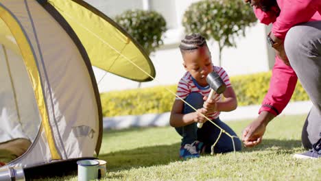 happy african american father and son pitching tent together in sunny garden, in slow motion