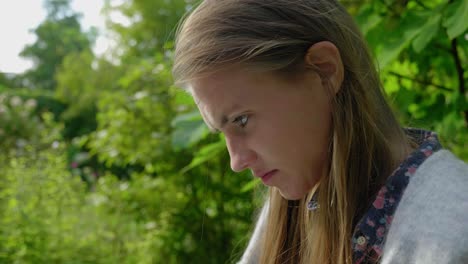 Slow-motion-close-up-shot,-from-the-side,-of-an-attractive-young-woman-reading-in-a-lush-green-garden-environment