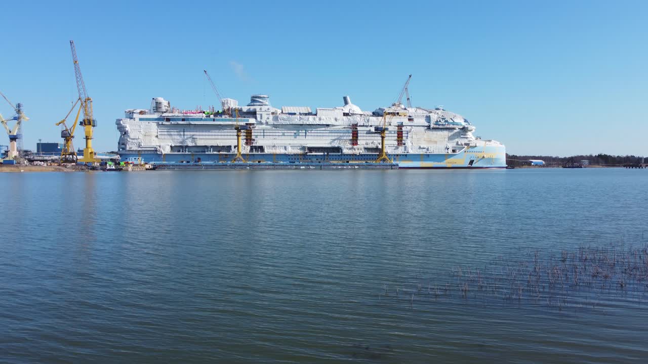 Large unfinished cruise ship at shipyard on a sunny day. Dolly forward drone shot
