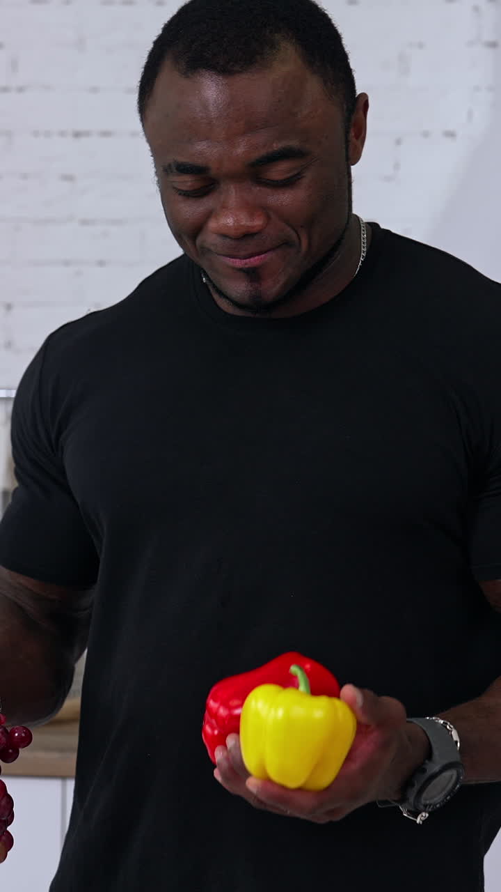 Sporty fit African man in the kitchen. Black male holding fruit and vegetables in his hands. Healthy male offering fresh vegetables. Vertical video