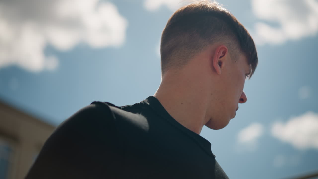 젊은 남성의 제스처, 활발한 움직임이 있는 캐주얼한 거리 풍경, 여름 구름과 도시 환경 속에서 자발적인 행동, 금속 울타리 근처 여름 하늘 아래 젊은 남성의 자발적인 제스처