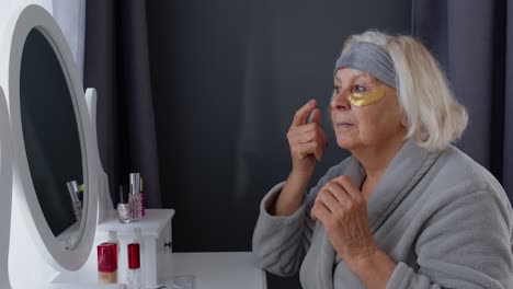 Abuela-Anciana-Cuidando-La-Piel-Cerca-De-Los-Ojos-Y-Las-Arrugas,-Maquillándose-En-Casa