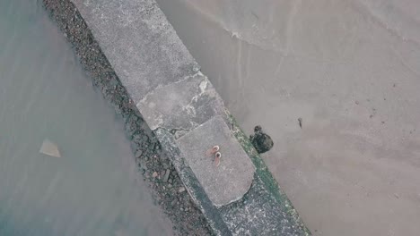 shoes on seascape while rising tide gradually engulfing sandy shoreline near wooden pier during bright summer day