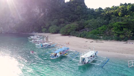 aerial: tourists boats at helicopter island tropical beach, el nido philippines