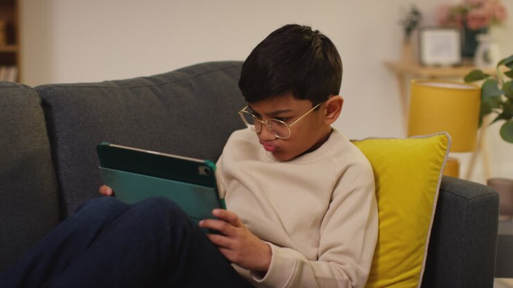 Close Up Of Young Boy Sitting On Sofa At Home Playing Games Or Streaming Onto Digital Tablet 11