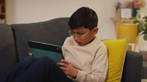 primer plano de un niño sentado en el sofá en casa jugando juegos o transmitiendo a una tableta digital 11
