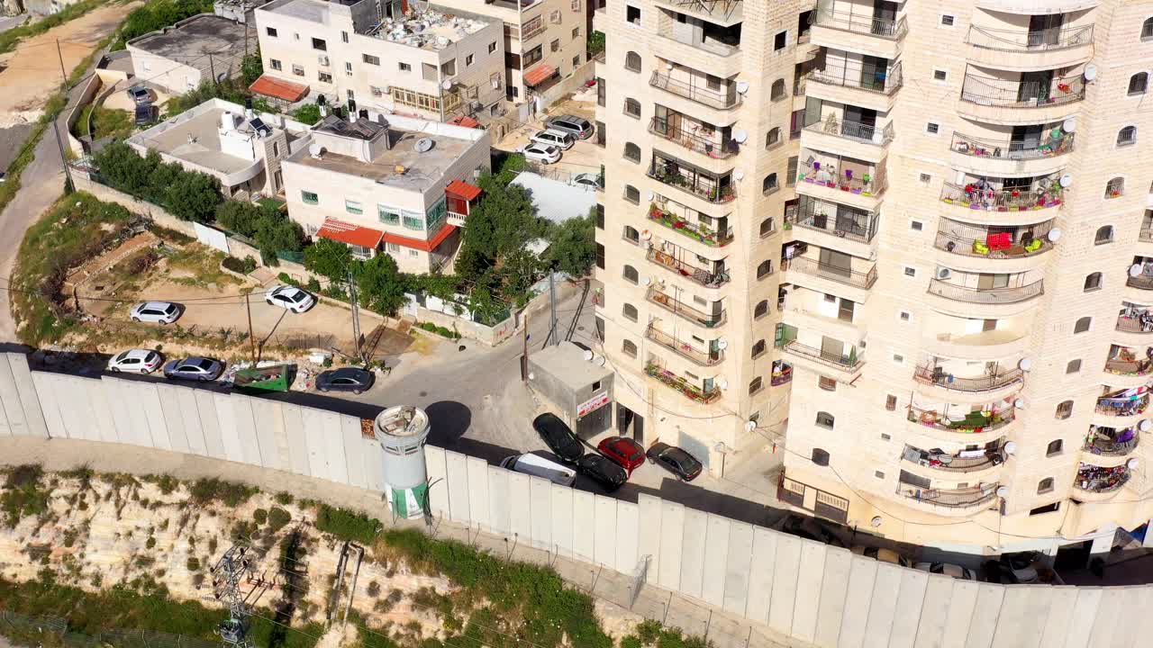 Aerial view of a multi-story apartment building alongside a concrete separation wall in an urban setting