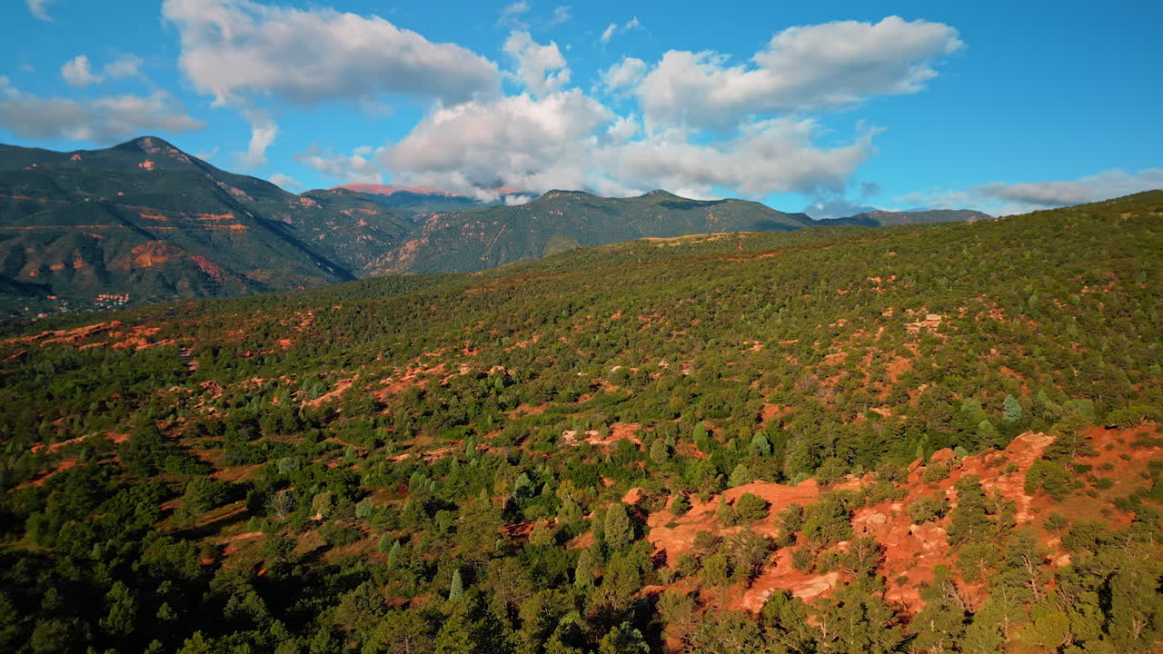 Rocky landscape covered with green trees and bushes. Fluffy clouds are in the blue sky above. Colorado Springs, Colorado, USA. Aerial view