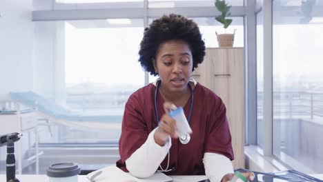 Doctora-Afroamericana-Sosteniendo-Medicamentos-Haciendo-Videollamadas-En-El-Consultorio-Del-Hospital,-Cámara-Lenta