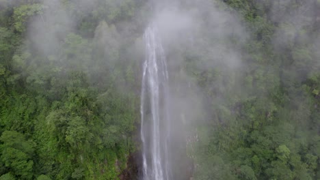 aerial pan left of clouds over las lajas waterfall streaming down a rocky pond surrounded by rainforest, san luis morete, costa rica