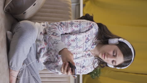 Vertical video of Sad and unhappy young woman listening to music at night at home.