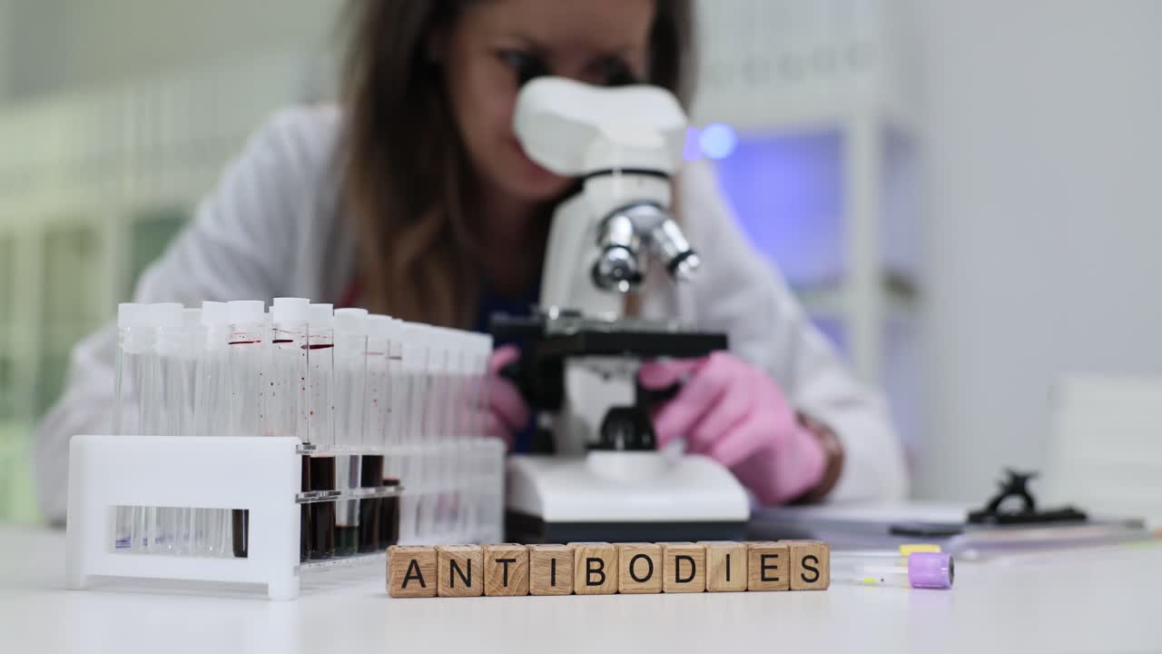 Scientist examining samples under a microscope in a laboratory with 'Antibodies' spelled out