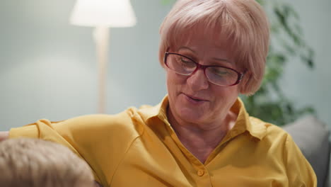 positive mature woman talks to toddler boy sitting on sofa