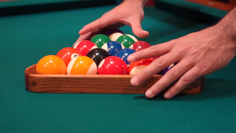 person racks 8 ball pool triangle closeup on the spot with solid and stripped billiard balls on table with blue felt or cloth and tightens rack with hands before lifting wooden triangle