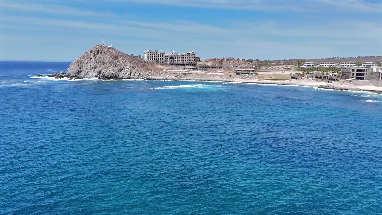 Un drone si avvicina dall'oceano aperto verso il capo Cabo del Sol, rivelando la spiaggia, le scogliere frastagliate, il Faro El Encanto e gli hotel costieri che si estendono lungo la costa a mezzogiorno.
