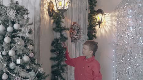 blond-boy-child-in-red-shirt-adjusts-pine-decor-with-cones