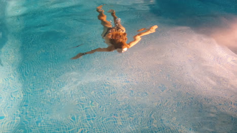 toma en cámara lenta de una mujer joven nadando sola dentro de una piscina por la noche