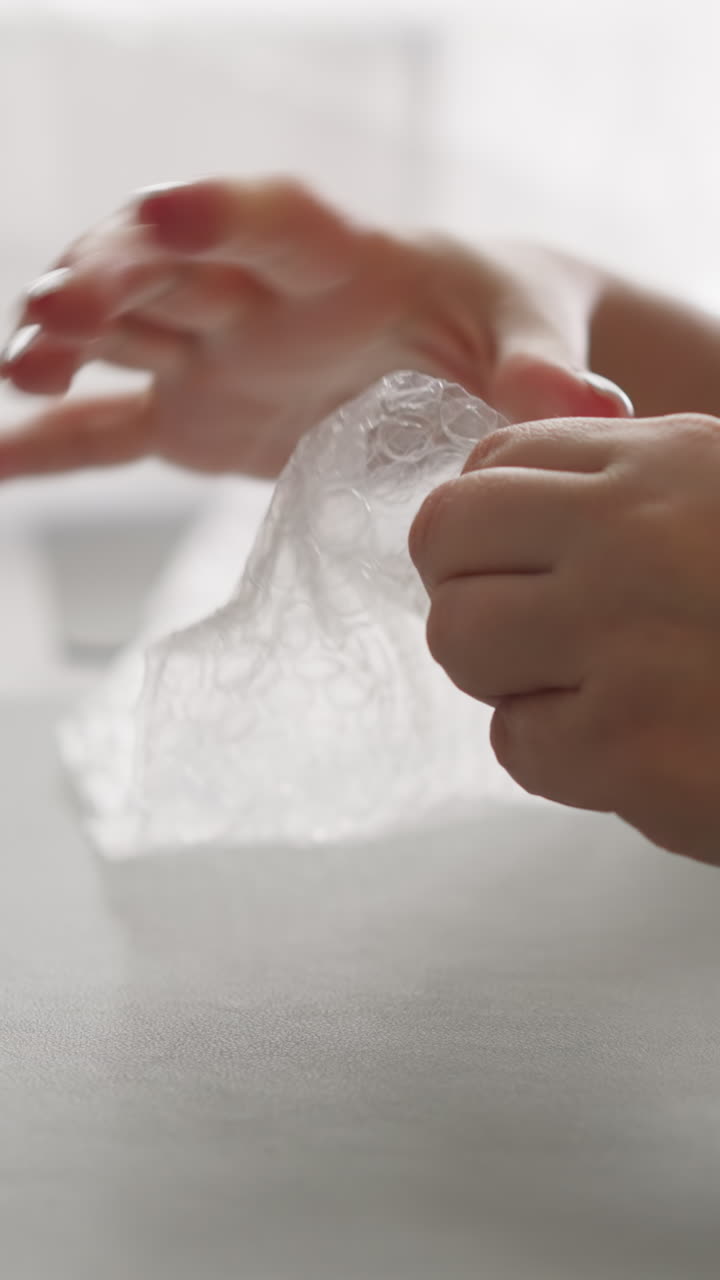 manos femeninas con uñas blancas presionan la película protectora haciendo estallar burbujas. mujer joven pasa su tiempo libre sentada en la mesa de la cocina con recipientes de comida de cerca