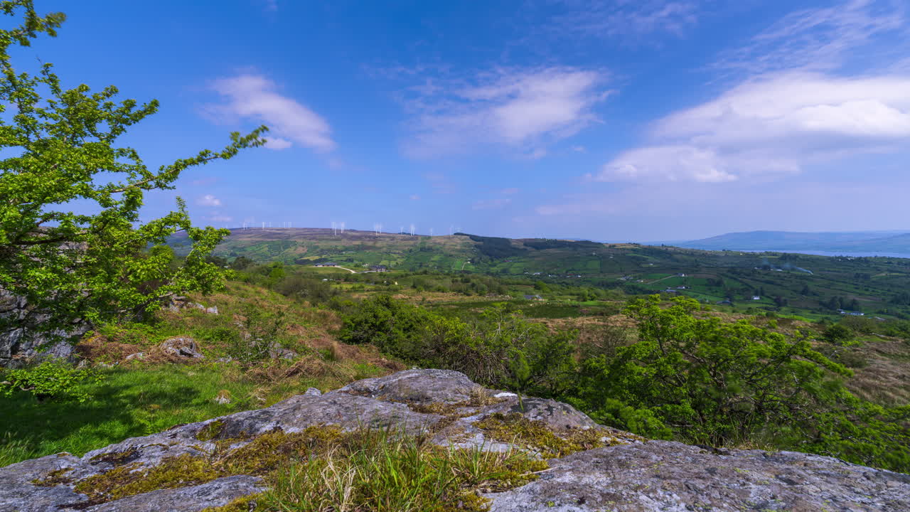 Time lapse of rural landscape with a single tree in the foreground and hills and lake in the distance during spring sunny day in Arigna mountains in county Leitrim in Ireland