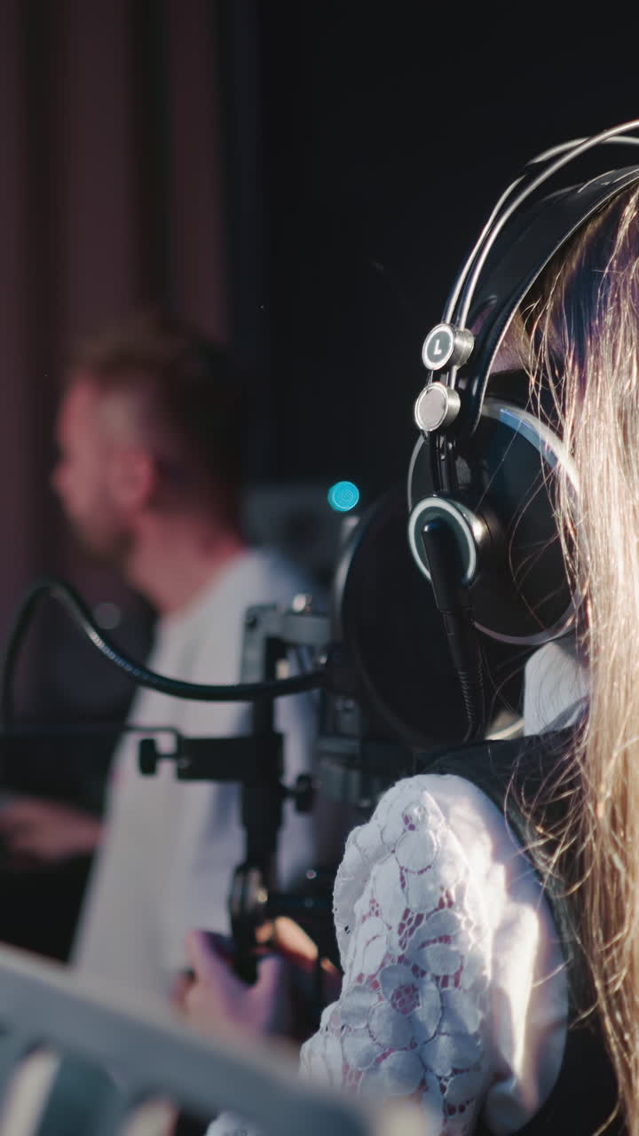 Girl sings following teacher in audio studio. Vocal teacher controls girl in headphones singing. Talented child prepares for performing in studio