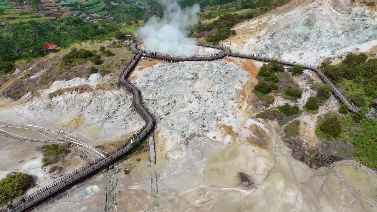 Drone flying forward to the volcanic activity at Sikidang Crater, a famous geothermal site in the Dieng Highlands, surrounded by lush greenery and hills