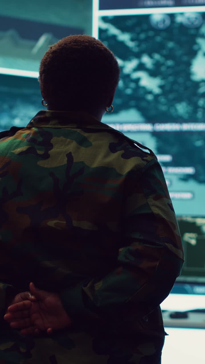 Soldatessa in uniforme mimetica che osserva schermi digitali