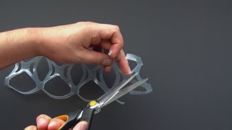 corte a mano con tijeras un par de anillos de seis paquetes o seis paquetes de yugos. anillos de plástico conectados utilizados en paquetes múltiples de bebidas sobre un fondo gris