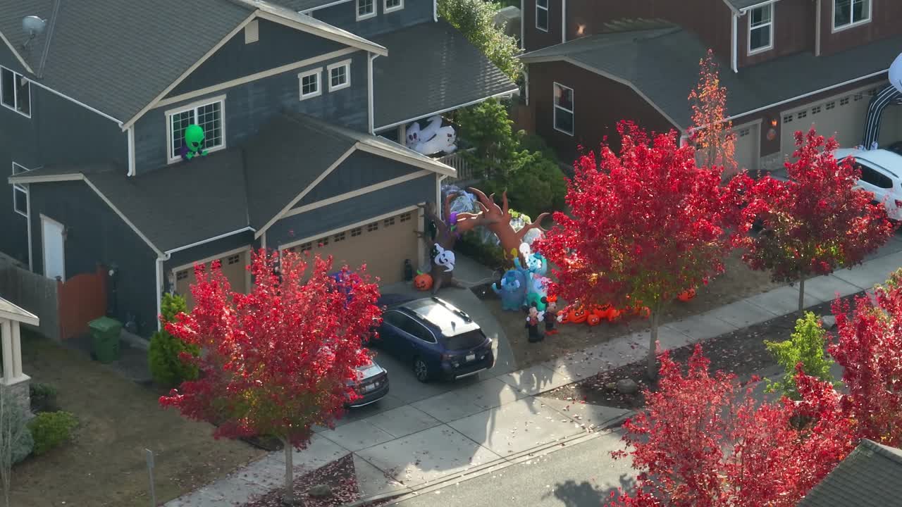 A suburban American home with a yard full of inflatables surrounded by red leaves in the trees