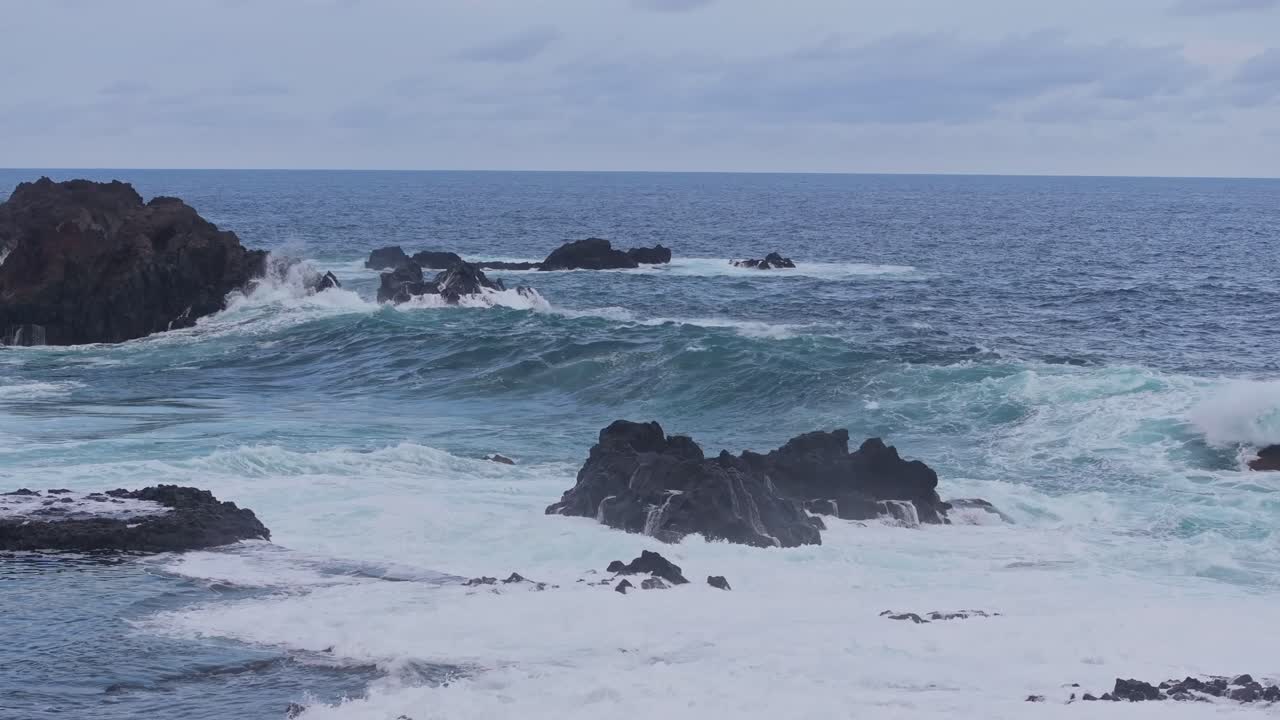Massive blue waves break violently against volcanic rocks before sunrise, Spain
